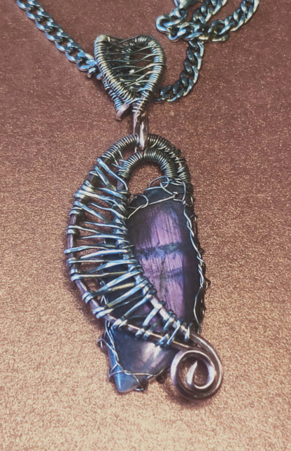 A photo of a pendant which is in the shape of a harp, with a leaf-shaped blue and purple laboradite nestled inside.