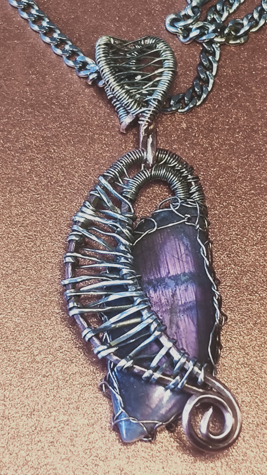 A photo of a pendant which is in the shape of a harp, with a leaf-shaped blue and purple laboradite nestled inside.